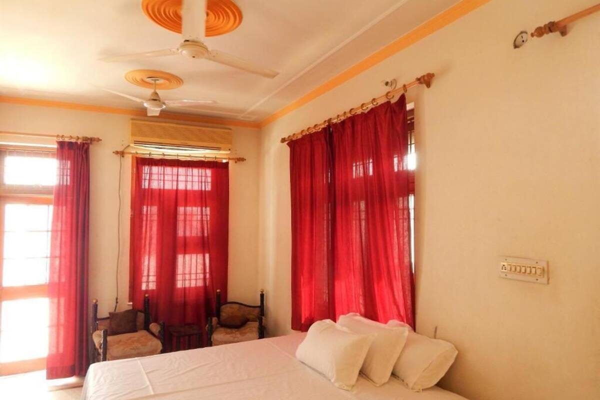 Ein Schlafzimmer mit einem Bett, roten Vorhängen, einem Deckenventilator und einem Fenster mit Jalousien.