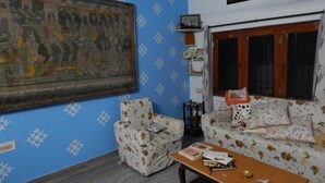 A living room with blue walls, a large painting, two patterned sofas, a wooden coffee table, and a window with a view. - VISHAL VILLA  (Jaipur)
