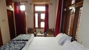 A hotel room with two beds, a table with a kettle, and a view of the street through the window. - VISHAL VILLA  (Jaipur)