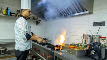 Un chef cocina con llama sobre una hornilla en una cocina con paredes de mármol y electrodomésticos de acero inoxidable.