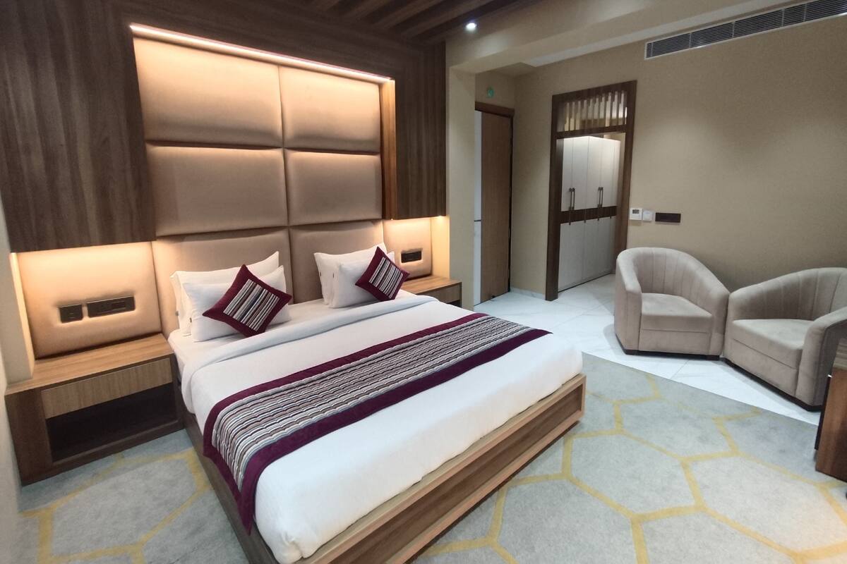 A modern bedroom with a large bed, a wooden headboard, bedside tables, a chair, and a wardrobe.