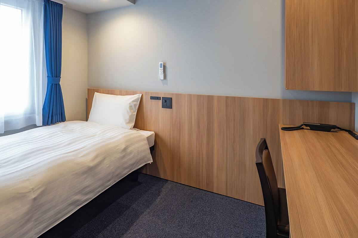 Quarto de hotel com uma cama, uma escrivaninha e uma cadeira.
