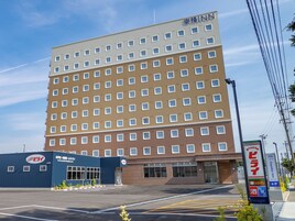 Um hotel de vários andares com fachada uniforme, céu claro e estacionamento à frente.