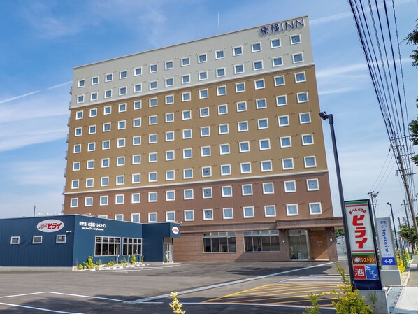 Un hotel de varios pisos con una fachada uniforme, cielo despejado y un estacionamiento al frente.