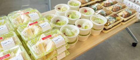 A table with various packaged food items, including sandwiches and salads, displayed on a wooden table in a commercial setting.