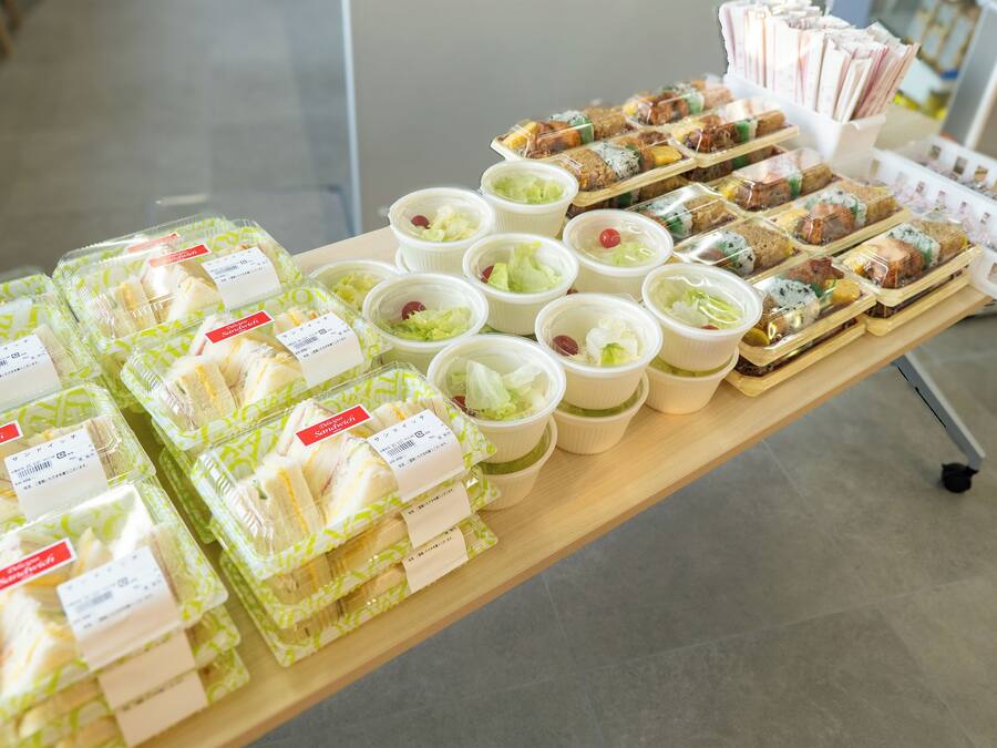 Una mesa con diferentes productos alimenticios envasados, incluyendo sándwiches y ensaladas, exhibida en un entorno comercial.