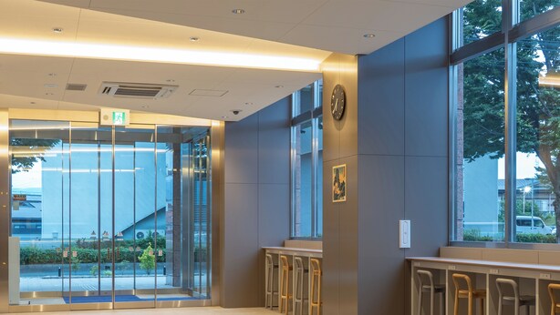 Eine moderne Lobby mit Glastür, Sitzgelegenheit und einer Wanduhr.