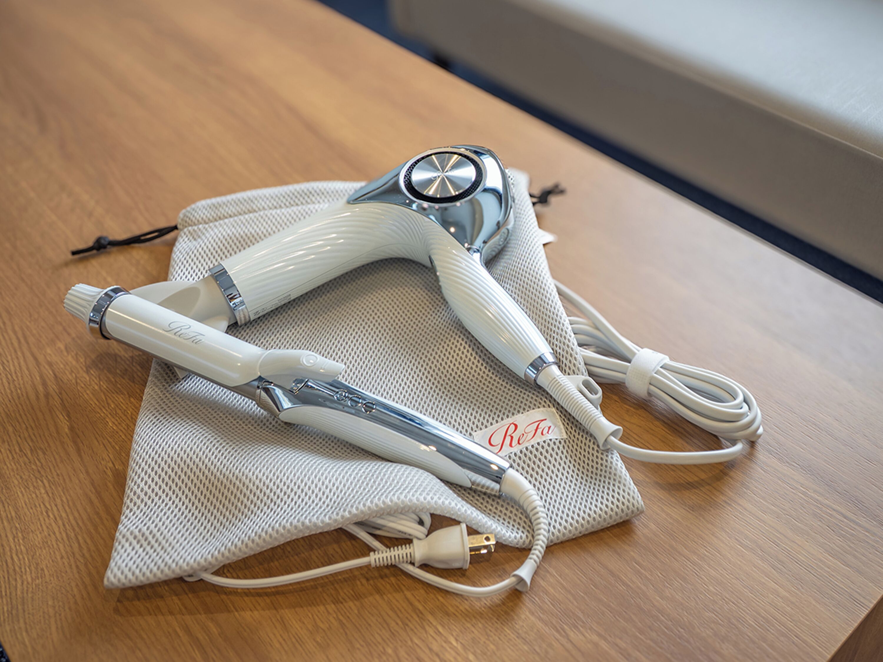 A pair of white hair straighteners on a beige mesh bag on a wooden table.