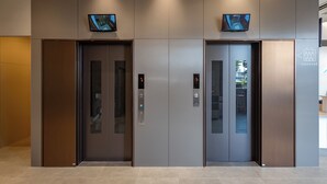 Zwei Aufzugtüren mit digitalen Anzeigen und einem Schild, das den Standort des Aufzugs kennzeichnet.