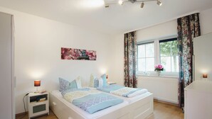 A bedroom with a bed, bedside tables, a window with curtains, and a radiator. - Vacation cottage Ditzum (Ditzum)