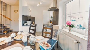 A modern kitchen with a dining area, wooden chairs, a clock, and a window with a view. - Vacation cottage Ditzum (Ditzum)