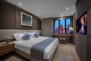 A hotel room with a large bed, a desk, a chair, a TV, and a window with a city view. - Chongqing Meirui Hotel (Chongqing)