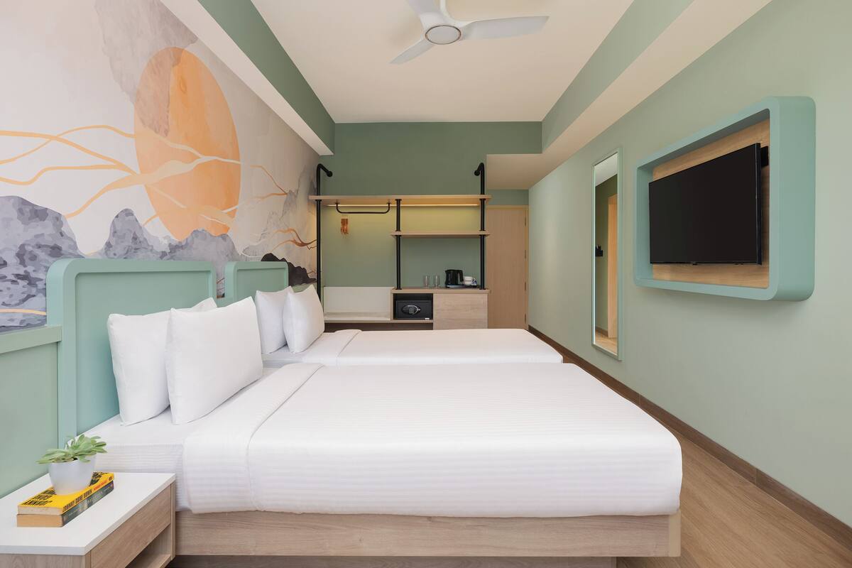 A hotel room with two beds, a flat-screen TV, a ceiling fan, and a mural on the wall.