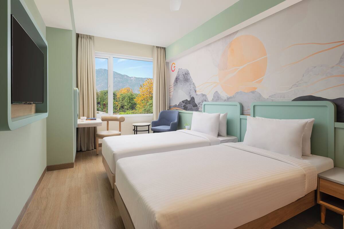 A hotel room with two beds, a TV, a desk with a chair, and a window with a mountain view.