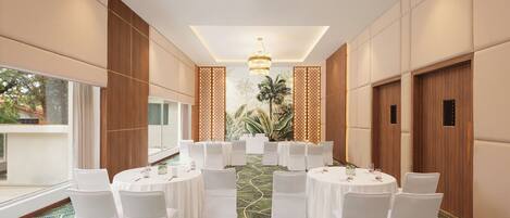 A conference room with round tables, white chairs, and a green patterned carpet.
