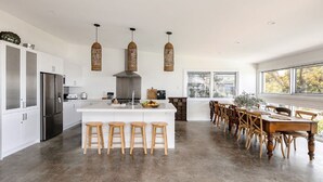 A modern kitchen with a central island, wooden stools, and a dining area with wooden chairs. - Stunning ocean views and pool (KILLCARE HEIGHTS)