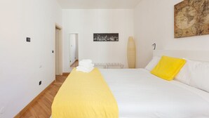 Une chambre à coucher comprenant un lit, une table de chevet, une lampe, une œuvre d’art accrochée au mur et une porte donnant sur une autre pièce.