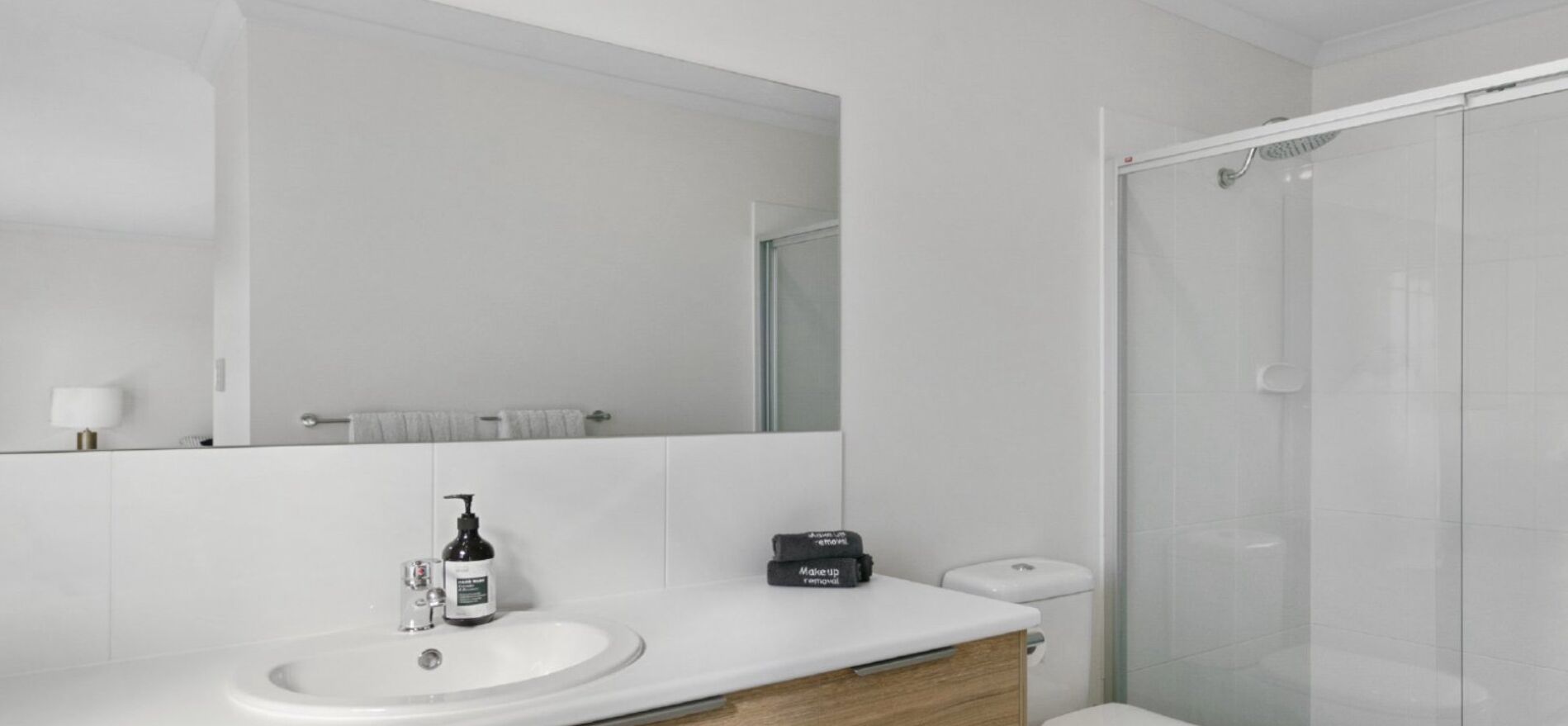 Een moderne badkamer met een wit wastafelmeubel, een spiegel, een handdouche en een toilet.