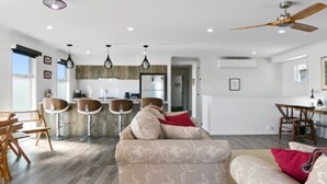 A modern living room with a sofa, a dining area with a table and chairs, a kitchen in the background, and a fireplace.