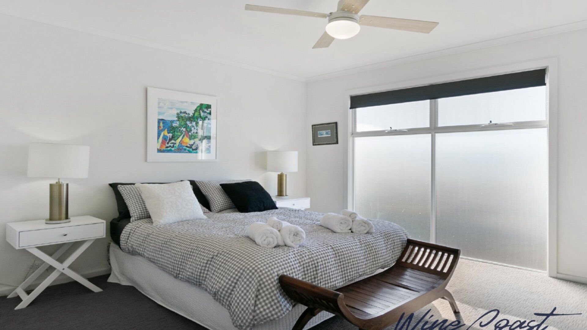 A bedroom with a bed, two bedside tables, a ceiling fan, a window with a view, and a chair.