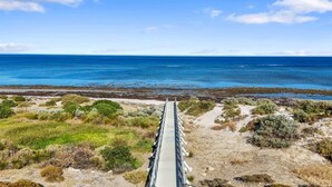 A coastal road leading to the sea with sparse vegetation and a clear sky.