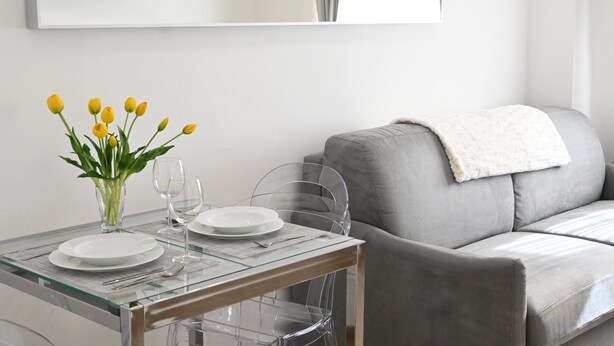 A dining area with a glass table, two plates, a vase with yellow flowers, and a grey sofa with a white throw blanket. - Spacious, luxury apartment with a view of the Duomo, accommodating 2+2+2 guests with privacy; rooftop elevator and Wi-Fi  (Firenze)