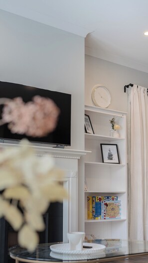 Cozy living room with a flat-screen TV above the fireplace, a bookshelf, and a round table.