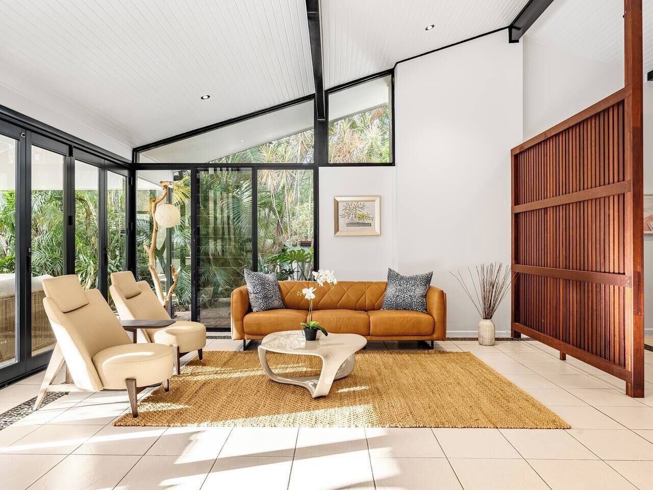 A modern living room with a sofa, two armchairs, a coffee table, and a large window with a view of greenery.