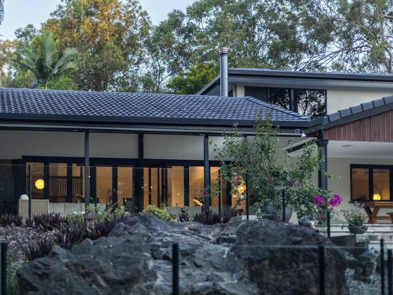 A modern house with a tiled roof, large windows, and a garden with rocks and plants.