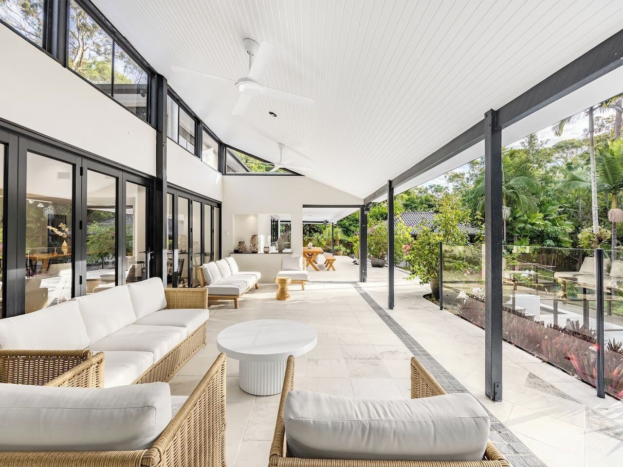A modern outdoor living area with a sofa set, round tables, and a view of the garden.