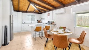 Une cuisine moderne dotée d’un îlot central, de meubles blancs et d’un coin repas avec des chaises marron.