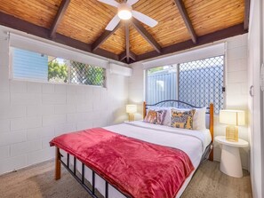 A bedroom with a bed, two bedside tables, a ceiling fan, and a window with a view.