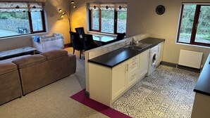 A compact kitchen with a central island, a dining area with a bench, and a washing machine. - Newcastle House Hotel (Ballymahon)