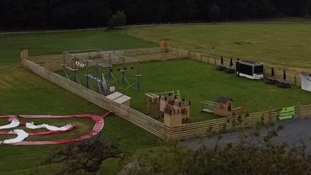 Un espace clos comprenant un petit bâtiment, une aire de jeux et une zone délimitée par une clôture avec une piste rouge.