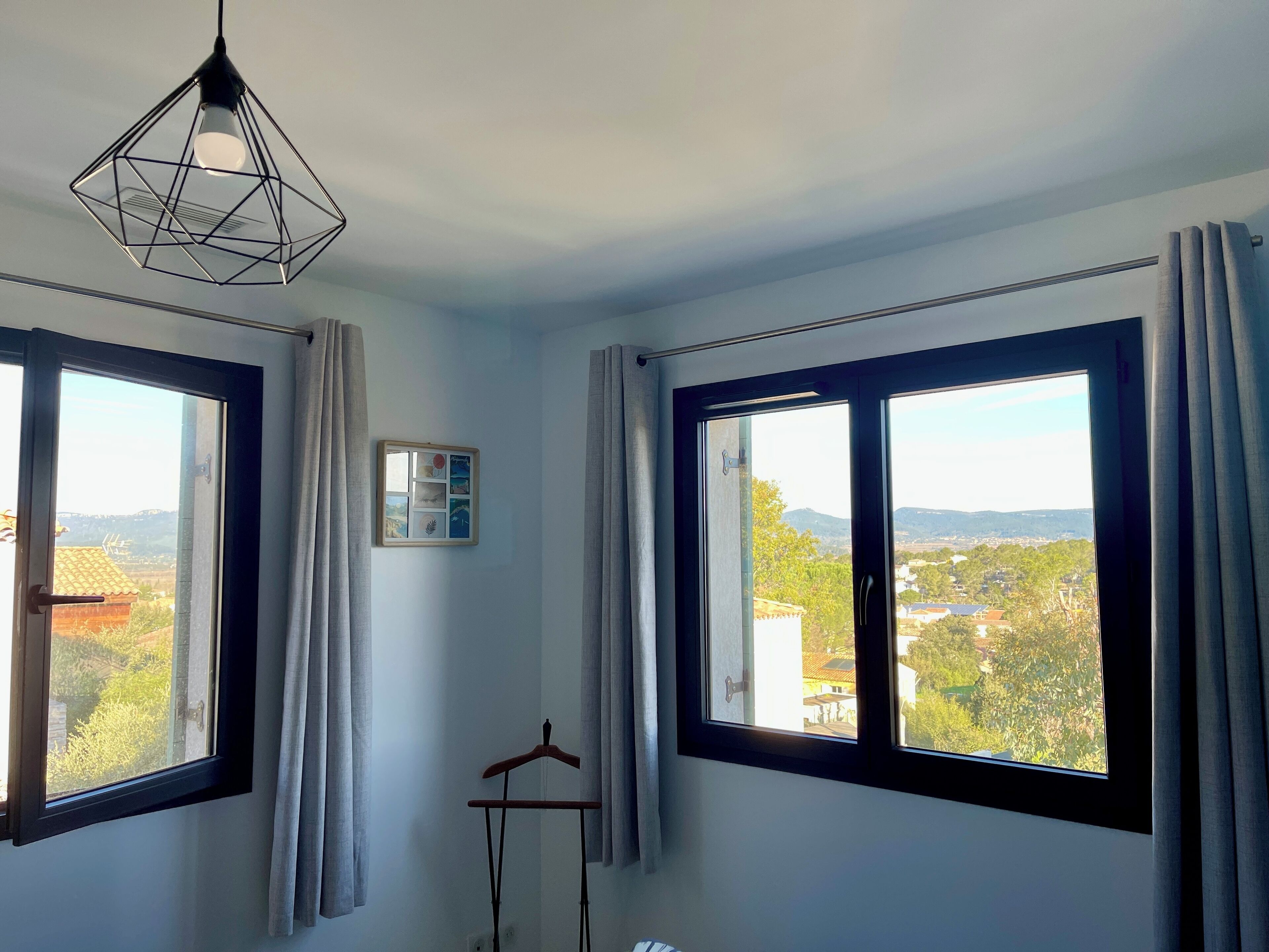 Ett rum med två stora fönster, en hängande lampa och en spegel som är monterad på väggen.