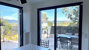 Ein Zimmer mit Tisch und Stühlen, große Schiebeglastüren führen zu einer Außenpatio-Terrasse mit Blick auf Bäume und Berge.