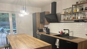 A modern kitchen with a wooden island, black cabinets, and a built-in oven. There is a window with a view of the outdoors, and a shelf with jars. - Spacious country house, 15 min from Bordeaux city center (Latresne)