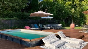 A swimming pool with lounge chairs and umbrellas, surrounded by a wooden deck and greenery. - Spacious country house, 15 min from Bordeaux city center (Latresne)