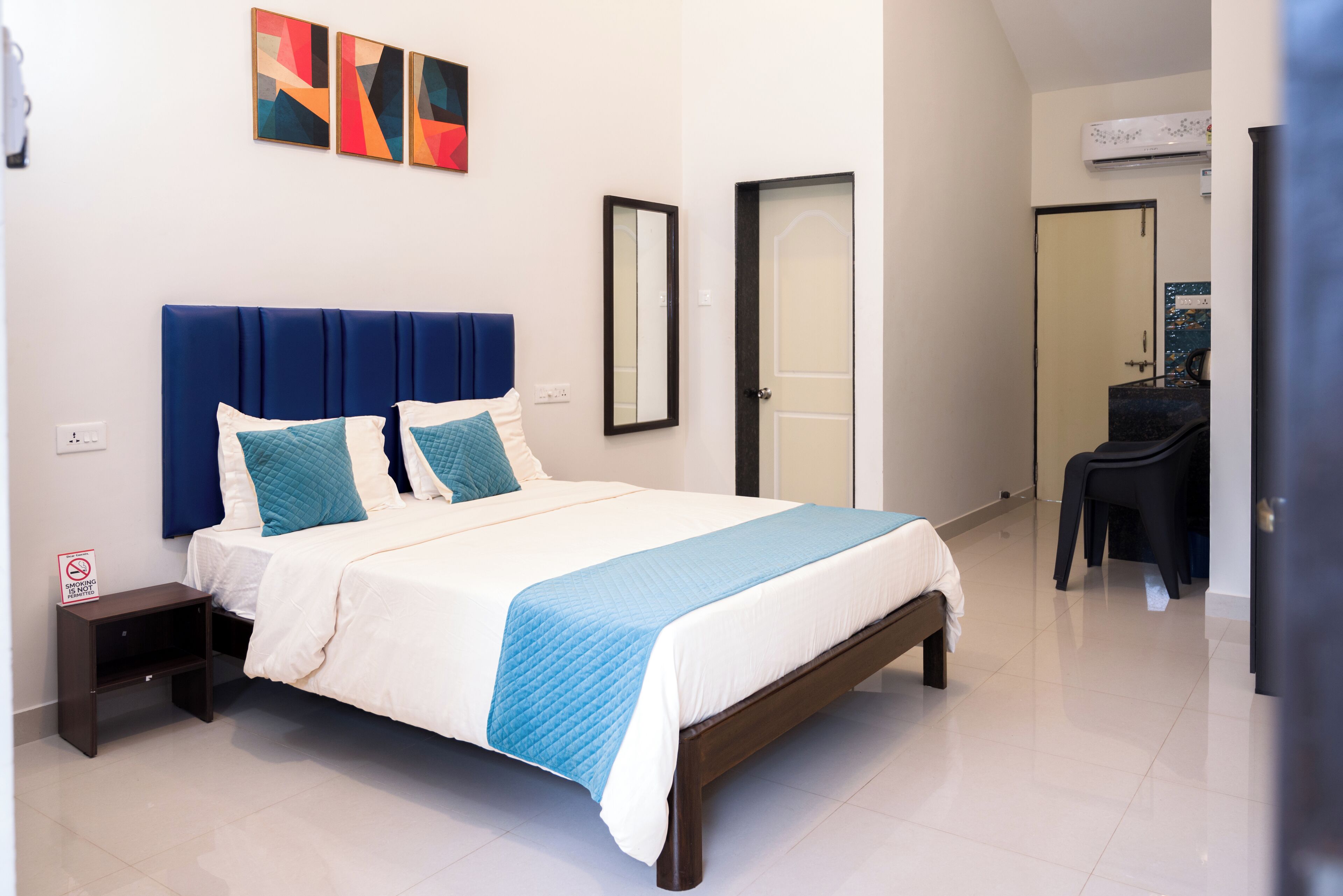 A neatly arranged bedroom with a bed, bedside tables, a mirror, and a door leading to another room.