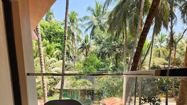 A balcony with a plastic chair, a glass railing, and a view of palm trees and a building in the background.