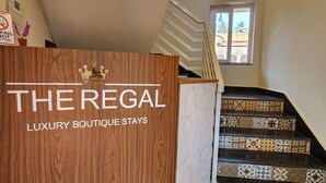 A staircase with patterned tiles leading to a landing with a wooden reception desk labeled "THE REGAL LUXURY BOUTIQUE STAYS".