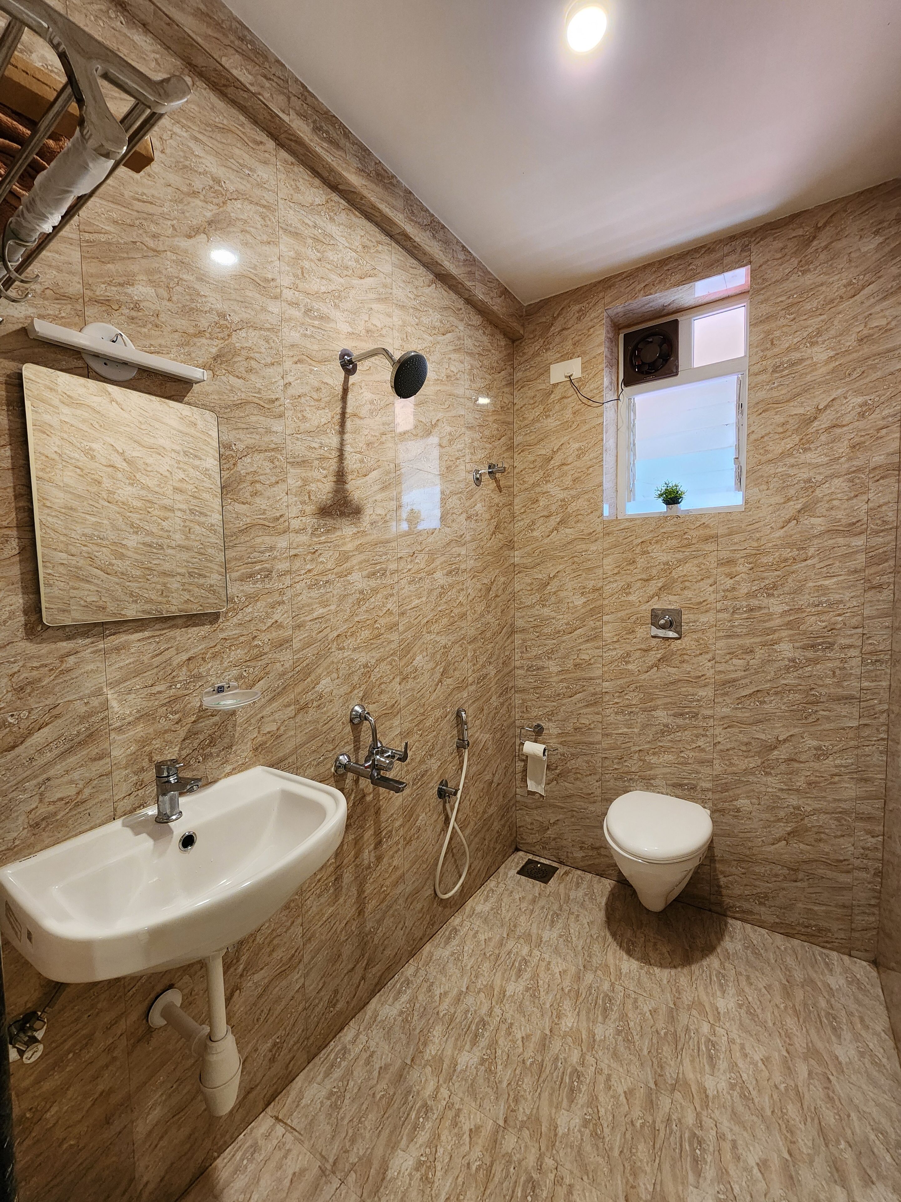 Un baño con pared de mármol, un lavamanos, un inodoro, una ducha y un ventanal pequeño.