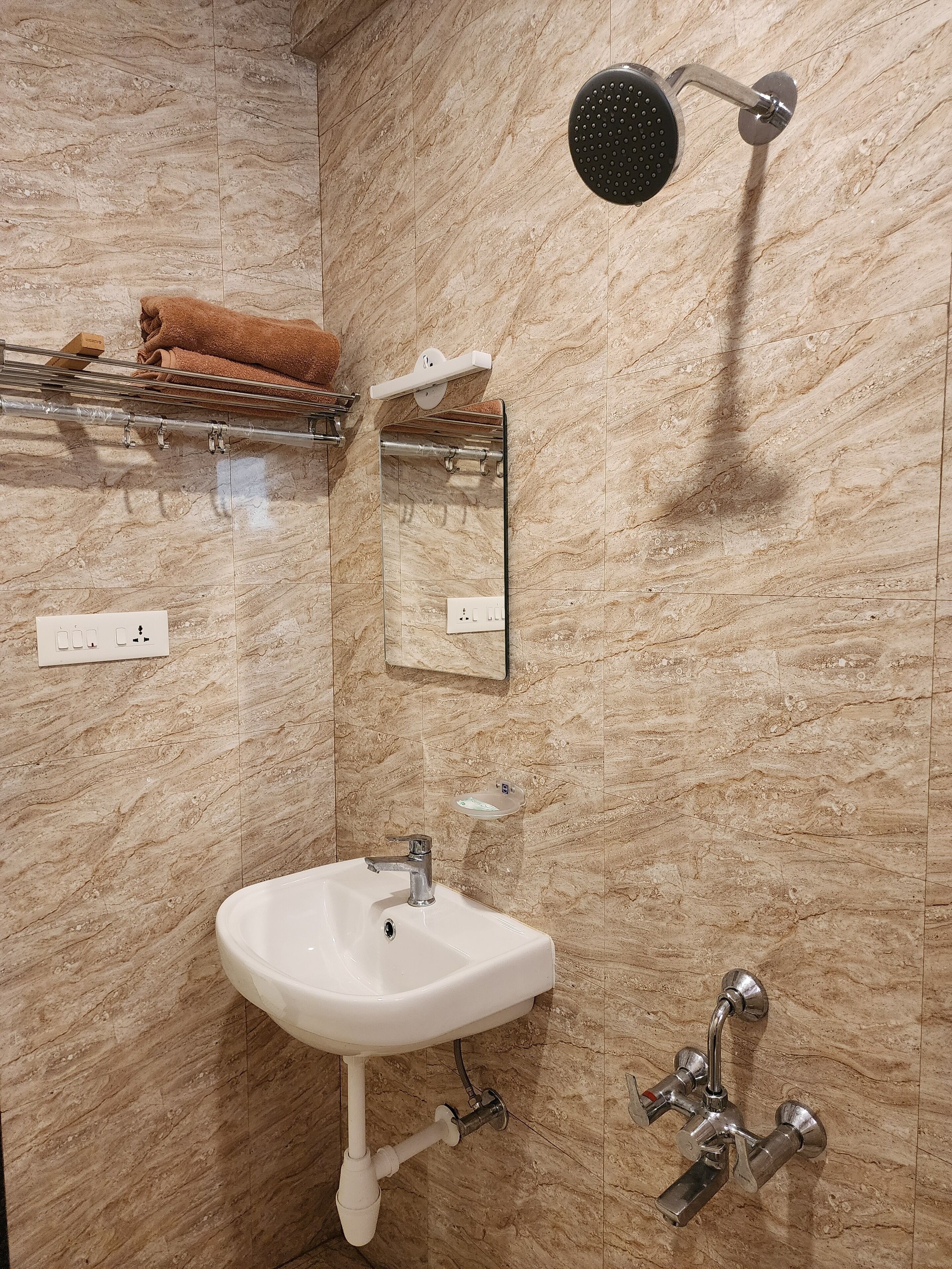 Casa de banho com lavatório branco, chuveiro manual, porta-toalhas com toalha castanha e espelho.