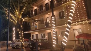 A multi-story building with balconies, string lights, and parked cars.