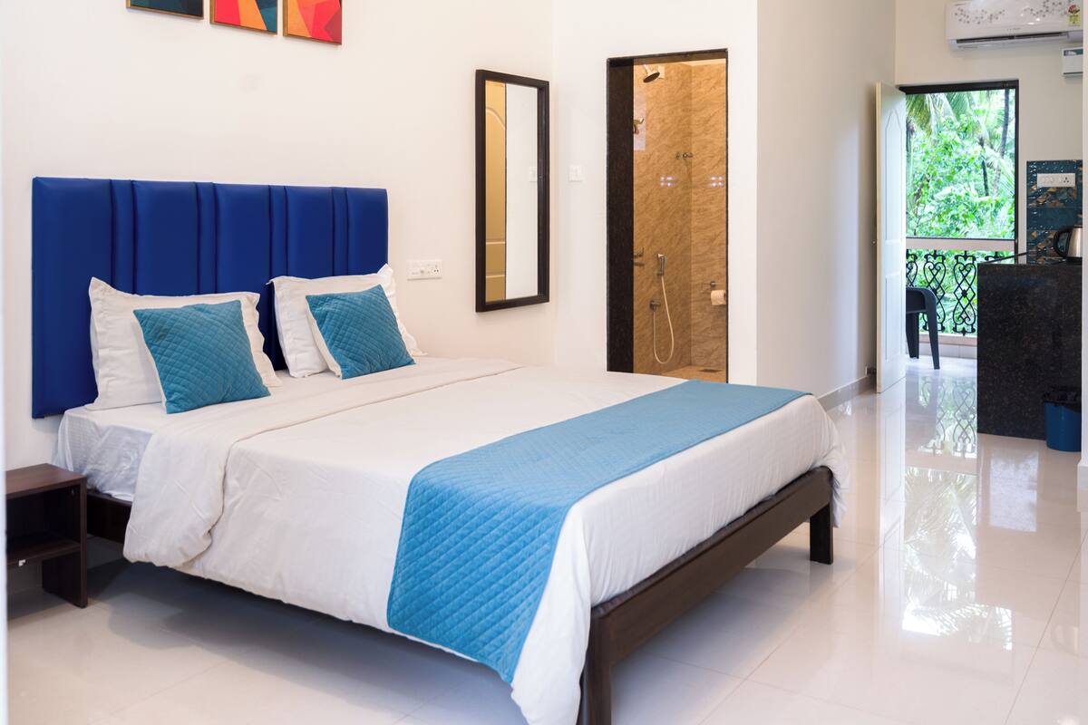 A neatly made bed with a blue headboard and white bedding, a wooden nightstand, and a large mirror on the wall.