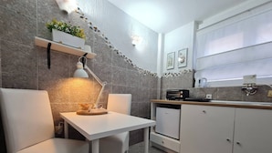 A modern kitchen with white cabinets, a white table, and two white chairs. There is a stone backsplash, a small plant, and a coffee machine. - Room-angelina Apartment 3 (Belgrade)