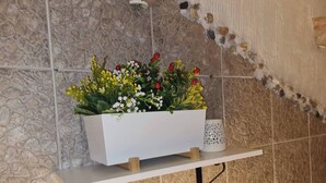 A white planter box with flowers on a white shelf against a textured stone wall. - Room-angelina Apartment 3 (Belgrade)