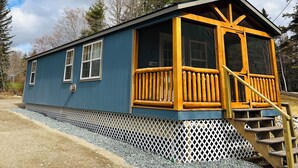 A blue cabin with a wooden porch and stairs leading up to a door.