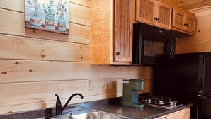 A wooden cabin-style kitchen with a double sink, wooden cabinets, a black refrigerator, and a microwave.