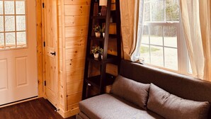 A wooden interior with a sofa, a ladder, and a window with curtains.